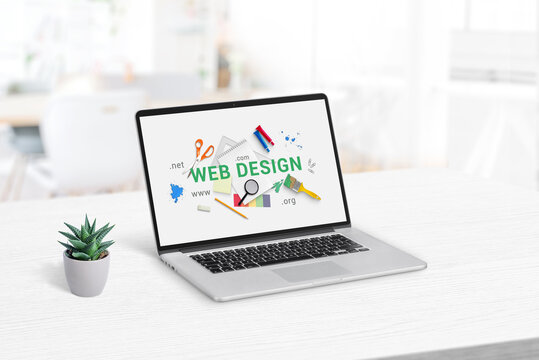 Web design studio concept page on laptop display. Clean office desk with plant beside