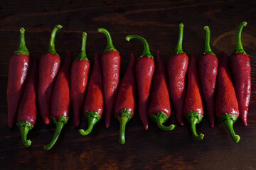 Closeup fresh wet red chili peppers in row on wooden table