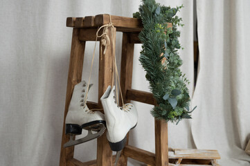 White vintage ice skates hanging on wooden stool, evergreen wreath and fabric background. Christmas interior decorations