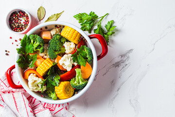 Vegan soup with broccoli, corn, cauliflower, peppers and sweet potatoes in saucepan. Cooking healthy food concept.