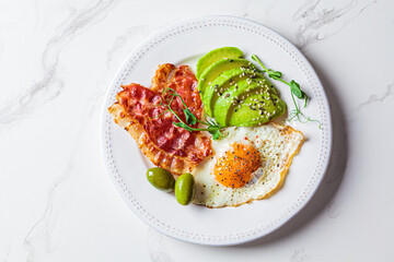 Keto breakfast concept. Fried egg with avocado and fried bacon in white plate.