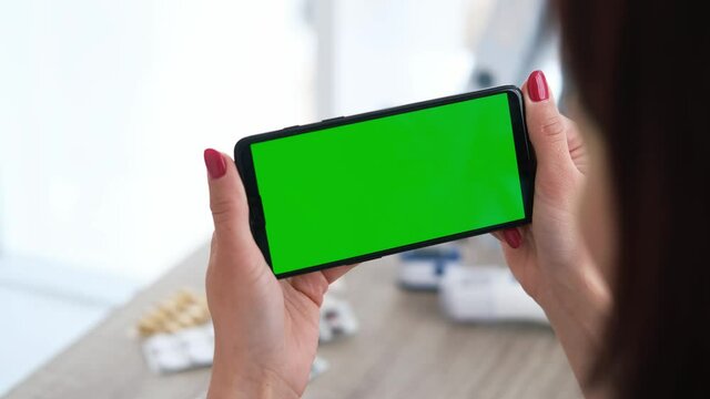 Woman doctor in the clinic looking something on screen of smartphone. Closeup view on cell phone with green display hands of healthcare specialist. Gren chromakey.