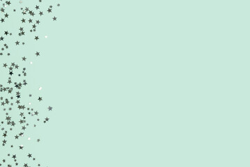 Glowing silver colored glittering stars confetti scattered on a turquoise background with place for text.