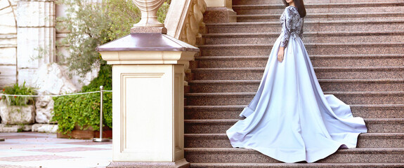 Banner with a stunning young woman in a gray elegant dresses on stone steps. Women's fashion. Festive clothing concept. Copy space on the left