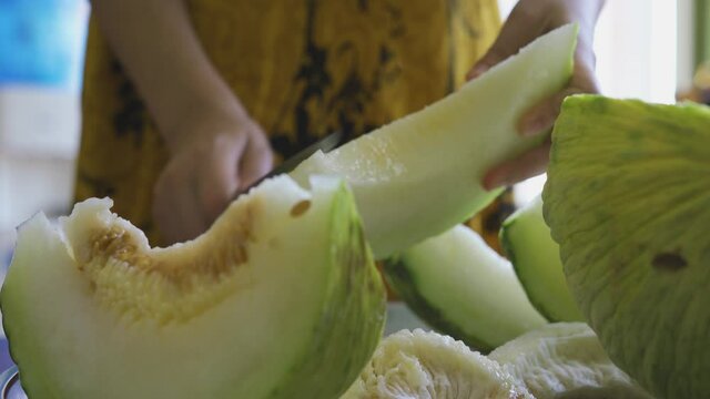Cutting exotic melon fruit. Close-up view of a woman hands slicing sweet melon. Hand of person cuts muskmelon