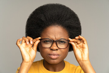 Young african woman with poor eyesight squinting eyes looking through eyeglasses try to read text....