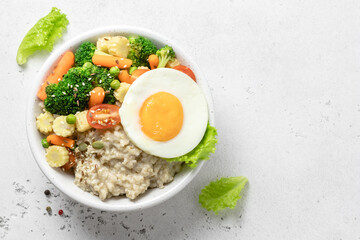Healthy breakfast savory oatmeal bowl with vegetables and egg. Space for text, top view.