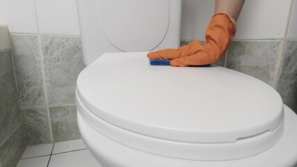 Cleaning toilet bowl. Housewife in rubber gloves cleans toilet with chemistry. Home house hygiene. A woman cleans a bathroom toilet. Hands with orange gloves cleaning a WC. Scrubbing toilet