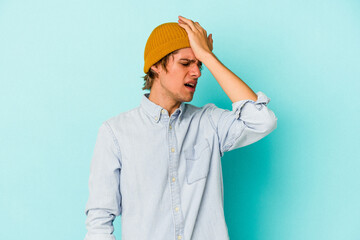 Young caucasian man with make up isolated on blue background  forgetting something, slapping forehead with palm and closing eyes.