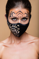close up of woman with tiger makeup and animal print protective mask posing isolated on beige