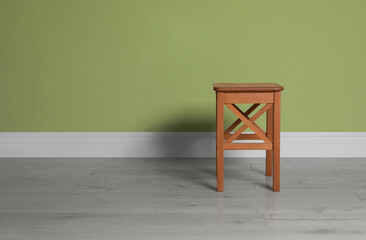 Stylish wooden stool near light green wall indoors. Space for text