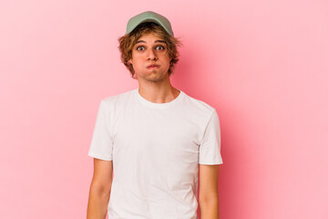 Young caucasian man with make up isolated on pink background blows cheeks, has tired expression. Facial expression concept.