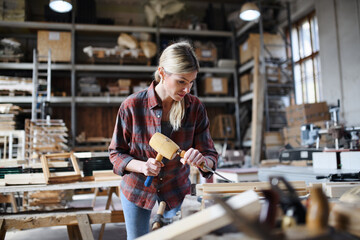 Portrait of female carpenter with goggles working on her product indoors in carpentry workshop. Small business concept.