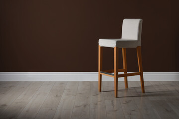 Stylish bar stool near brown wall indoors. Space for text