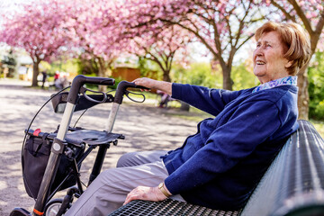 Seniorin sitzt allein im Park im Frühling auf einer Bank , den Rollator neben sich