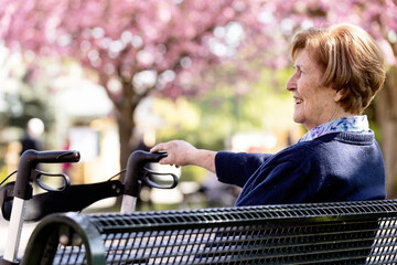 Seniorin sitzt allein im Park im Frühling auf einer Bank , den Rollator neben sich