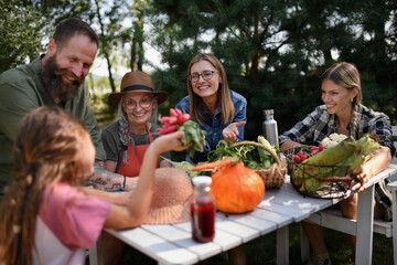 Family of farmers sitting by the table and looking at their harvest outdoors at community farm.