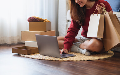 A woman using laptop for online shopping , holding shopping bags and opening postal parcel box at home