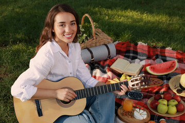 Happy young woman with guitar on plaid outdoors. Summer picnic
