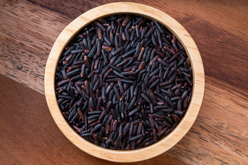 Rice berry grains in wooden bowl on wooden background, Black rice grains in wooden bowl on wooden background.
