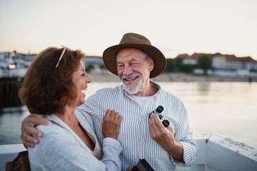 Happy senior couple hugging outdoors on pier by sea, looking at each otherand laughing.