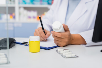 cropped view of pharmacist holding bottle with medication and writing on clipboard near blister packs