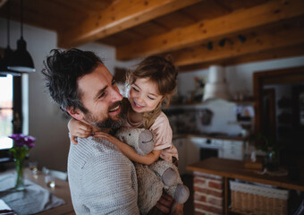 Mature father with small daughter standing indoors at home, holding and hugging.