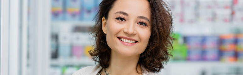 cheerful and tattooed woman smiling in drugstore, banner