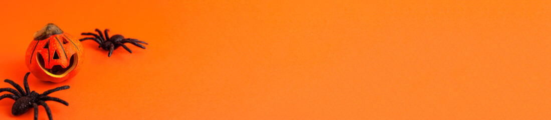 Close up of decoration orange small smile Halloween pumpkin and black horror spiders on orange blurred background and copy space. Holiday autumn concept backdrop