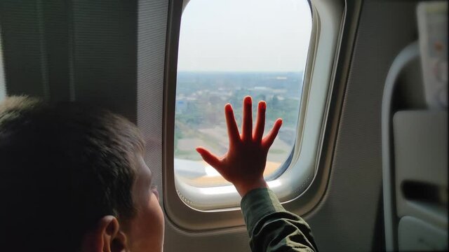 arrival at airport, child boy during the landing of plane put his hand on window and looks with interest at the landscape