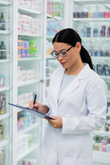 asian pharmacist in glasses writing on clipboard in drugstore
