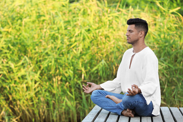 Obraz premium Man meditating on wooden pier outdoors. Space for text