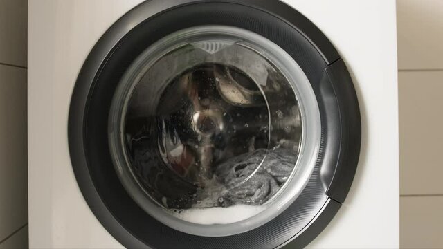 Washing machine working during laundry cycle with clothes inside. Front view