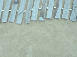 Wooden footbridge on a sandy beach. Uneven, damp wooden planks held together. The edge of the beach...