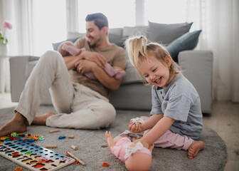 Happy young man taking care of his newborn baby and little daughter indoors at home, paternity leave.