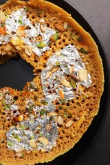 Rajasthani Ghevar. Ghewar is an Indian crunchy sweet dish made using refined flour, sugar, and ghee. Garnished with silver foil and dry fruits. Over dark background with copy space.