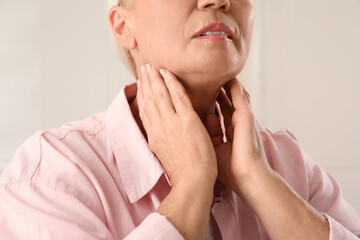 Mature woman doing thyroid self examination on light background, closeup