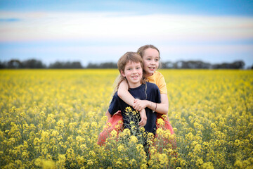 Fototapeta premium Brother and sister playing together in vibrant canola field in full bloom
