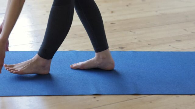 Closeup view of young woman unrolling mat before yoga practice in home room spbi. 4k video Pic of legs of female athlete rolls out object for training and walks on floor in light interior. Active