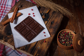 Bar of dark bitter chocolate with chilly pepper, cinnamon, red pea pepper flavour on white paper,...