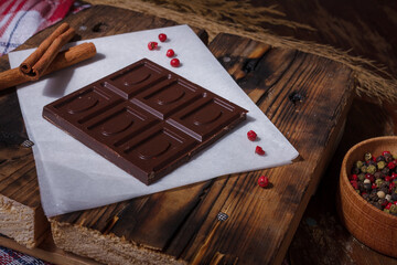 Bar of dark bitter chocolate with chilly pepper, cinnamon, red pea pepper flavour on white paper,...