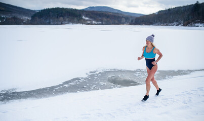 Active senior woman in swimsuit running outdoors in winter, cold therapy concept.