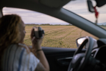 Woman inside her car taking a picture with her analog camera of a landscape in a rice field