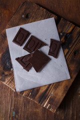 Broken bar of dark bitter chocolate with chilly pepper and red pea pepper inside on white paper, wooden board background. Unusual sweets taste