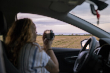 Woman inside her car taking a picture with her analog camera of a landscape in a rice field