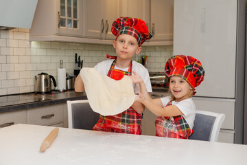 children in chef costumes roll out the dough with a rolling pin for Christmas cookies. brother and...