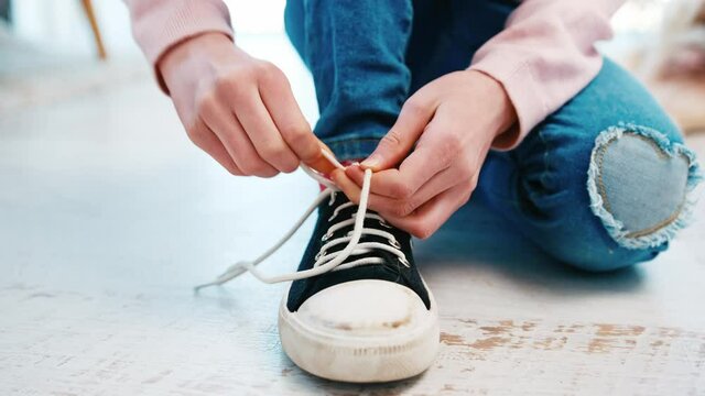 Child girl sitting on the floor and tying shoelaces on sneakers
