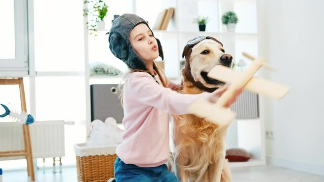 Portrait of little girl with wodden plain and golden retriever dog wearing pilot hats