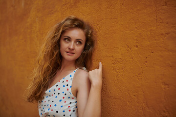 Portrait of young woman with orange hair on the street with an orange wall as a background
