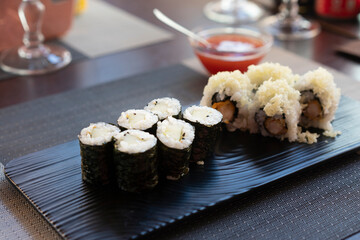 Traditional japanese rolls sushi with cucumbers and rolls sushi with shrimps fried on black plate at restaurant.